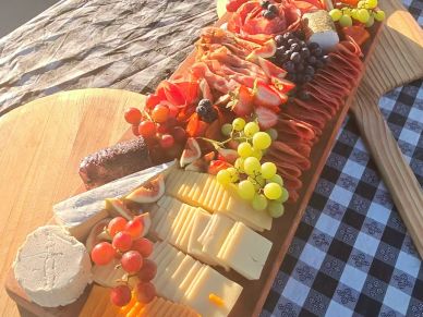 Wooden board with meats, cheeses, and grapes.