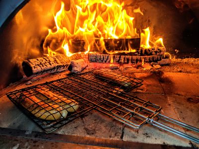 Wood-fired oven with bread baking on a grill rack in front of flames.