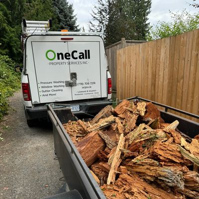 Truck and trailer loaded with wood chunks beside a wooden fence.