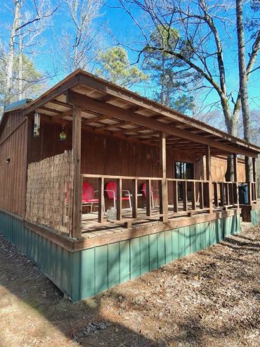 Wooden porch with red chairs on a rustic cabin surrounded by trees.
