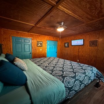 Cozy bedroom with wooden walls, blue doors, and a ceiling fan.