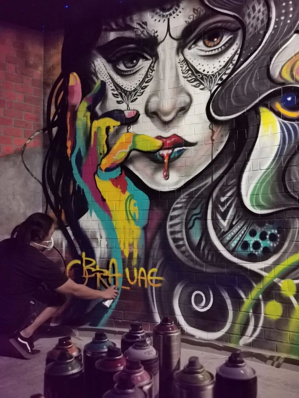 Artist painting vibrant street art of a woman's face on a brick wall.