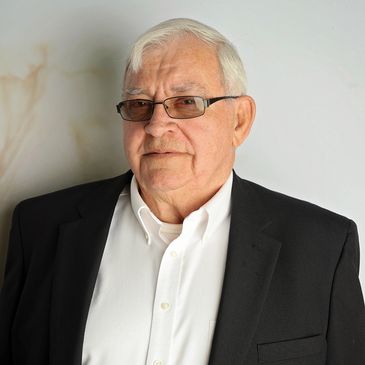 Elderly man in glasses wearing a black blazer and white shirt.
