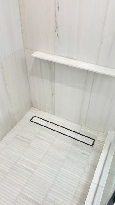 Modern white tiled shower floor with sleek linear drain.