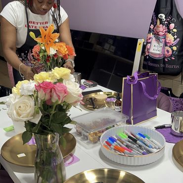 A woman arranges colorful flowers in a room with purple decor and gold plates.