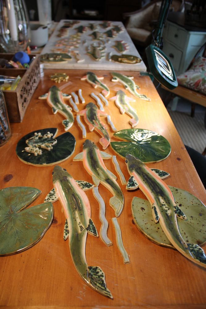 Ceramic fish and lily pad artworks arranged on a wooden table.