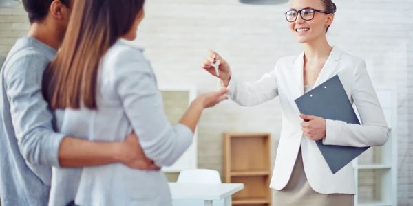 Professional Woman is handing a key to a man and woman for their rental property.