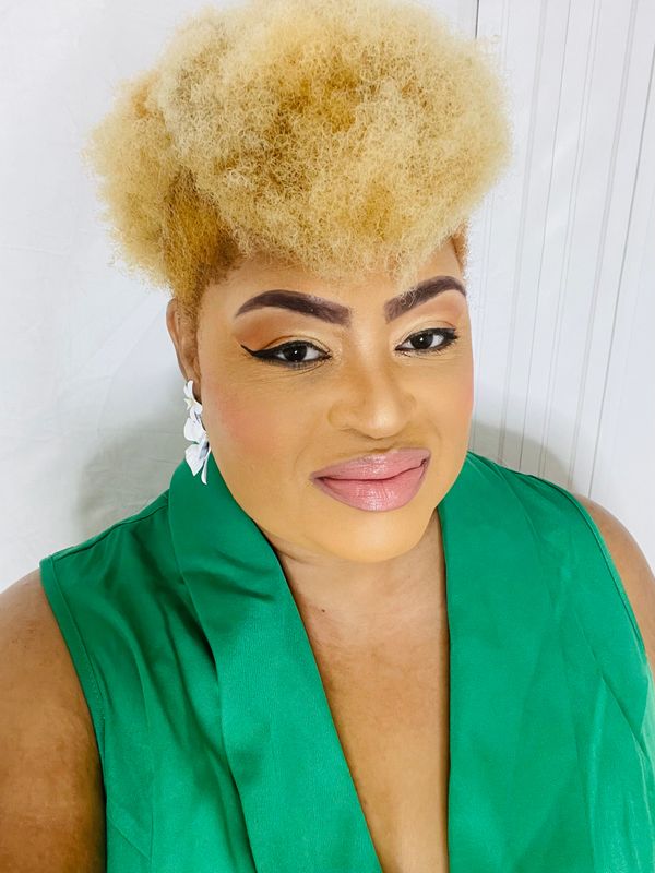 Woman with blonde afro and green outfit smiling at the camera.