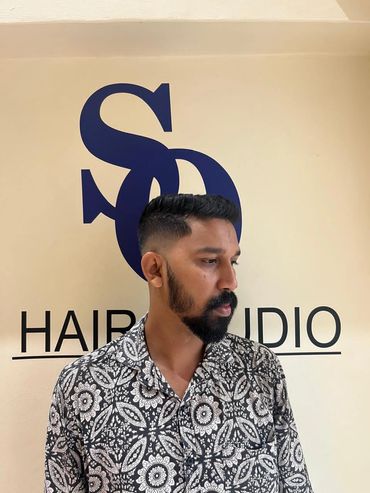Man with a fresh haircut and beard in front of a hair studio sign.