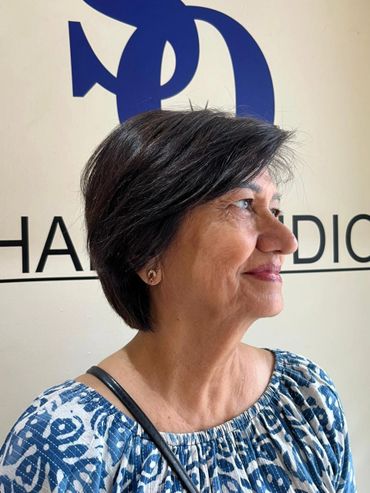 Side profile of a smiling woman with short dark hair and a blue-patterned blouse.