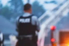 Blurred image of a police officer standing near emergency lights.