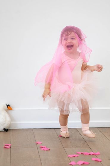 A joyful toddler dressed in a pink tutu and veil, dancing happily.