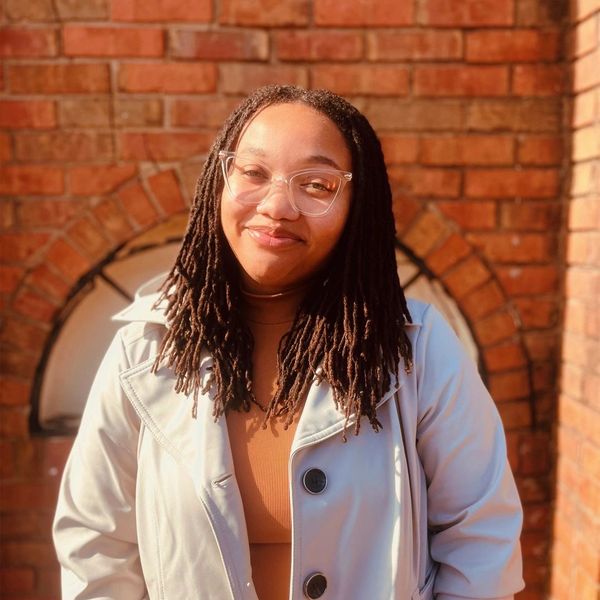 Woman with dreadlocks smiling in front of a brick wall.