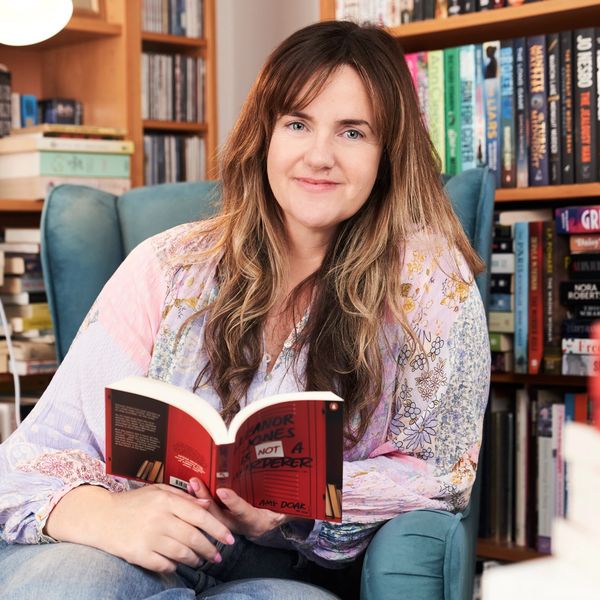 Woman reading a book while sitting in a cozy chair surrounded by bookshelves.