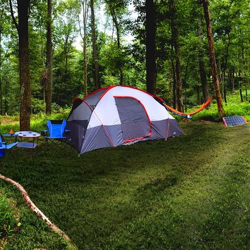 Camping tent set up in a forest clearing with hammock and solar panel.