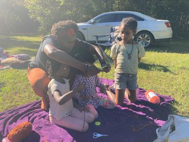An adult teaching kids how to knit outdoors.