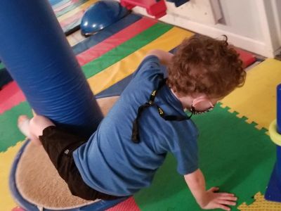 Child playing on colorful padded floor in a gym or therapy room.
