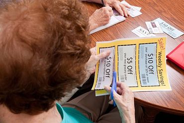 An elderly person cutting out weekly savings coupons at a table.
