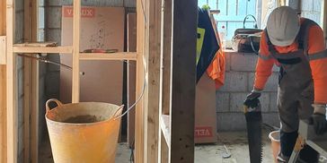 Construction worker sawing wood in an unfinished room.