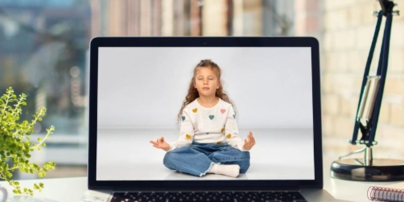Young girl meditating on a laptop screen in a cozy workspace.