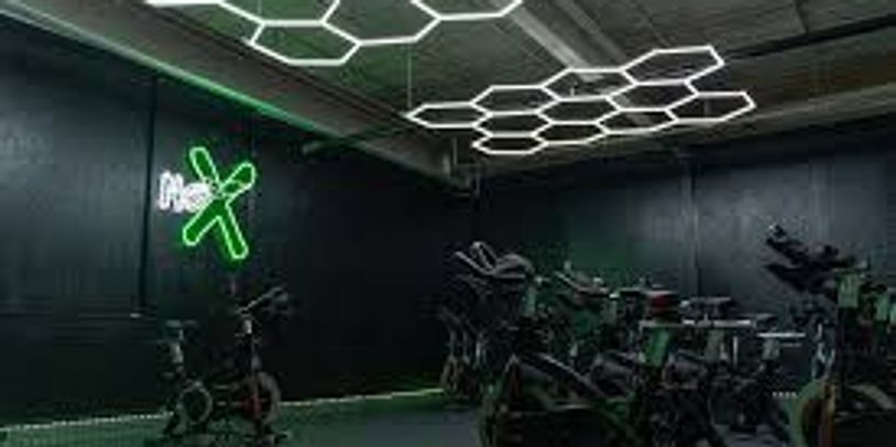 Modern indoor cycling studio with neon lights and hexagonal ceiling design.