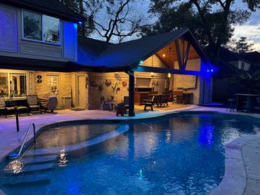 Cozy backyard with a lit swimming pool and covered patio at dusk.