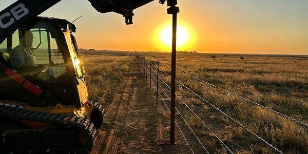 Machine installing fence posts during sunset in a rural area.