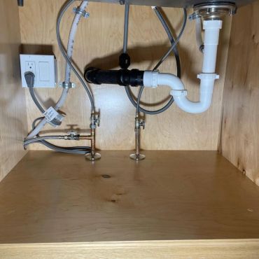 Under-sink plumbing pipes and valves in a wooden cabinet.