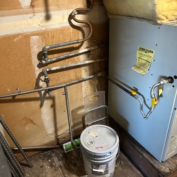 Old water heater with rusted pipes and a bucket on wooden floor.