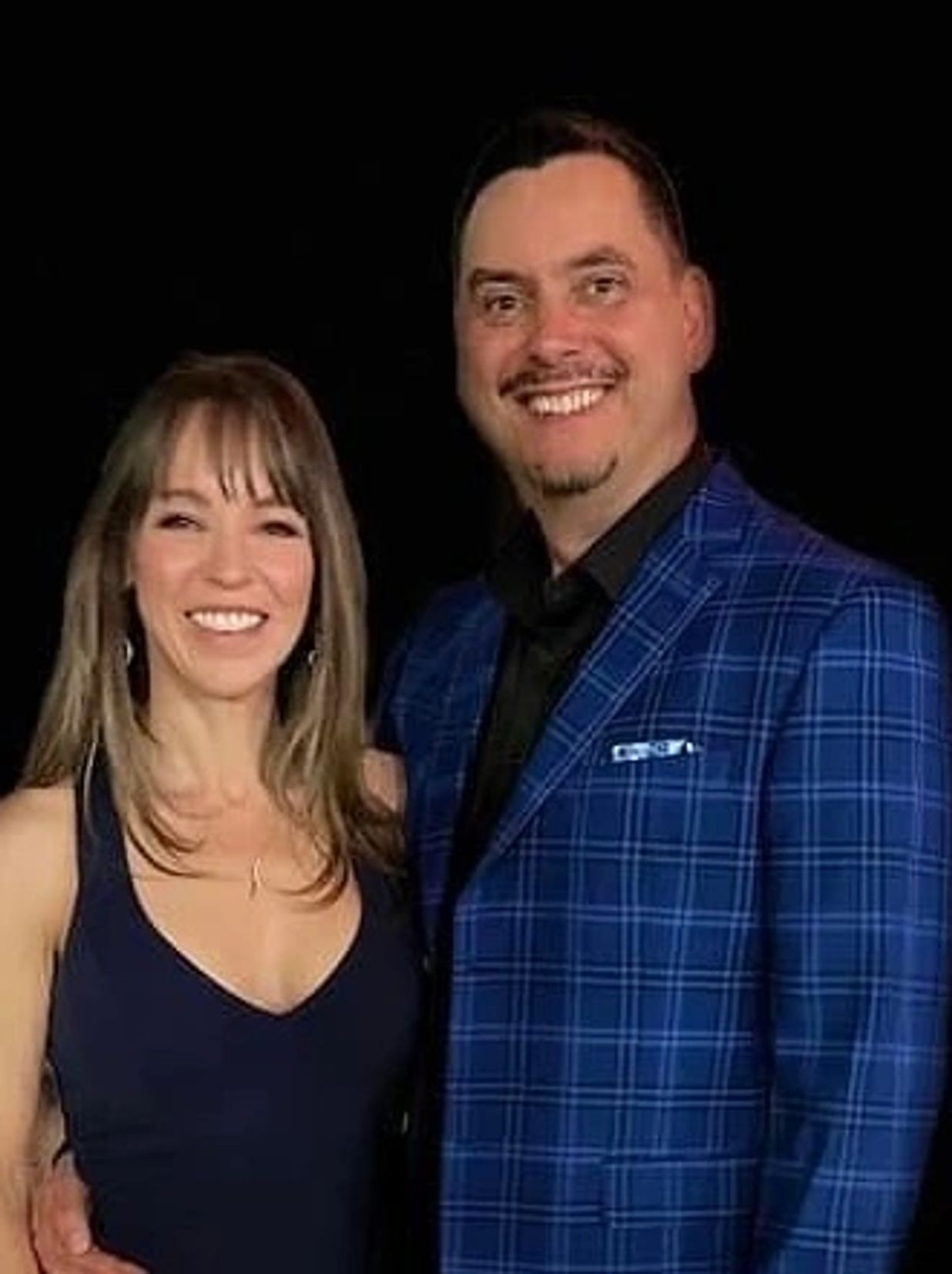 A smiling couple dressed elegantly against a black background.