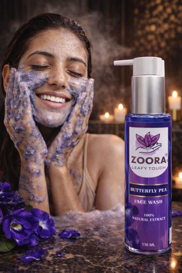 A woman happily applying Zoora Butterfly Pea face wash with purple foam.