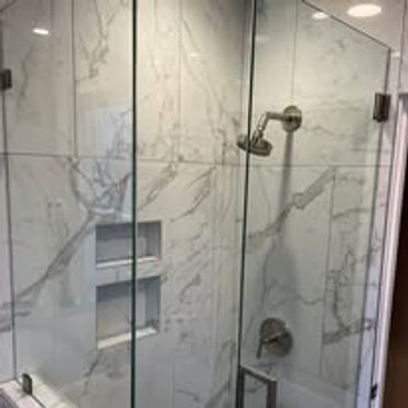 Modern marble shower with glass doors and built-in shelves.