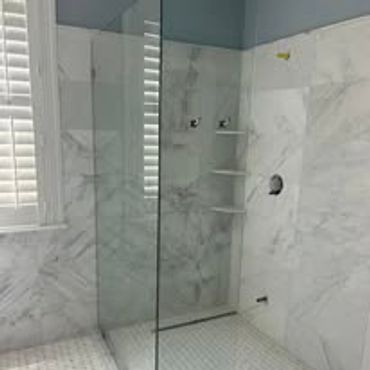 Modern bathroom shower with glass door and marble tiles.