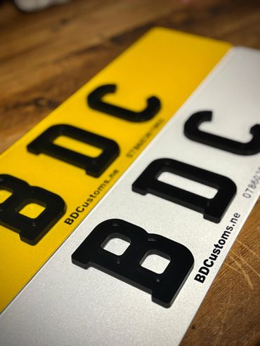 Close-up of two custom vehicle license plates with black raised characters.
