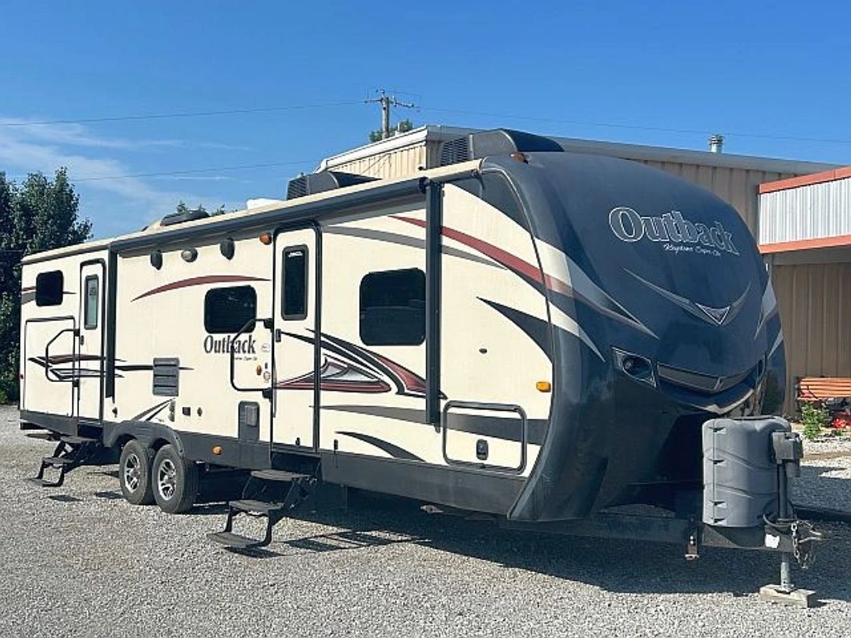 A large Outback travel trailer parked on gravel with clear skies.