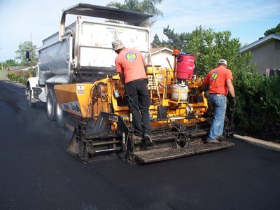 Asphalt paving crew riding on the back of an asphalt paver while paving community road