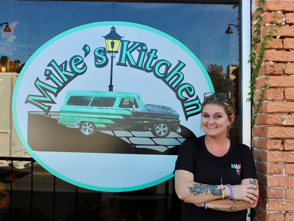 Smiling woman standing next to a window sign for Mike's Kitchen.