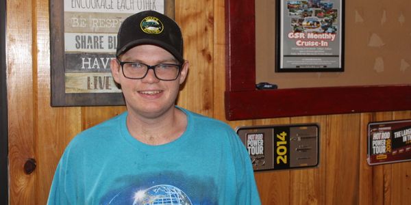 A smiling young man in a Universal Studios Florida shirt and black cap indoors.