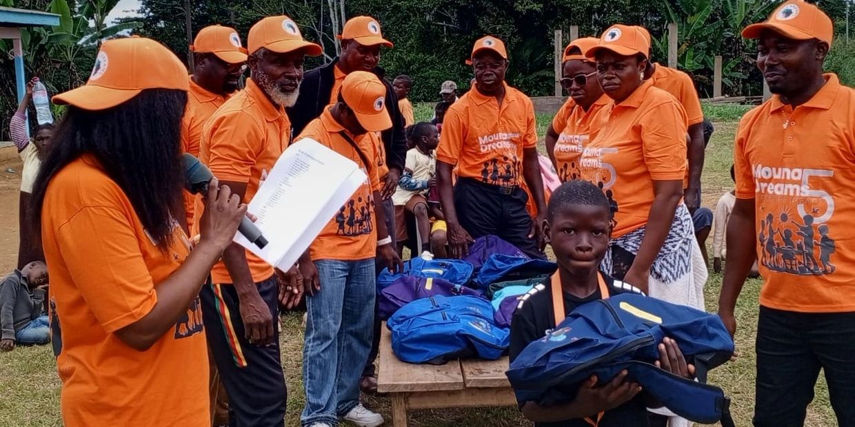 Group in orange shirts distributing backpacks to children outdoors.