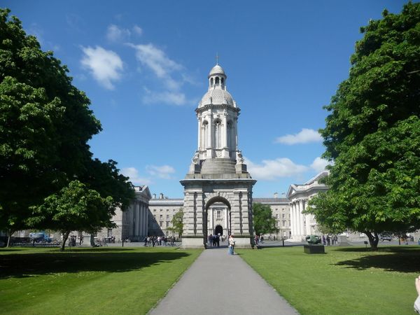 Historic bell tower centered on a pathway with green trees and blue sky.