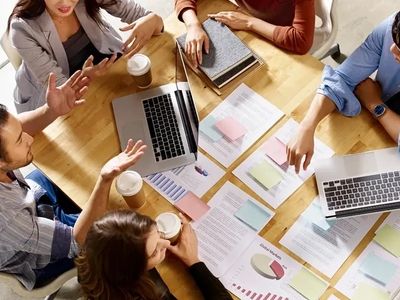 Group of people collaborating at a desk with laptops and coffee.
