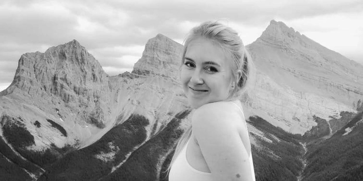 Smiling woman posing with majestic mountain peaks in the background.