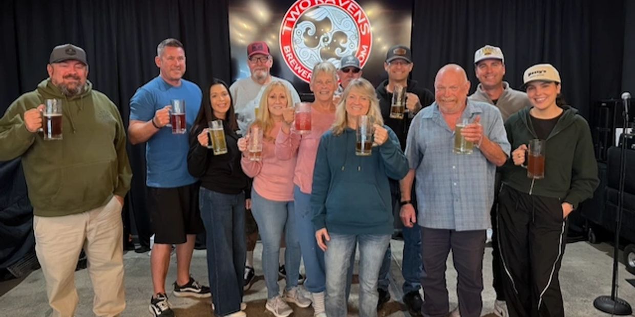 Group of people holding beer mugs and smiling at a brewery event.