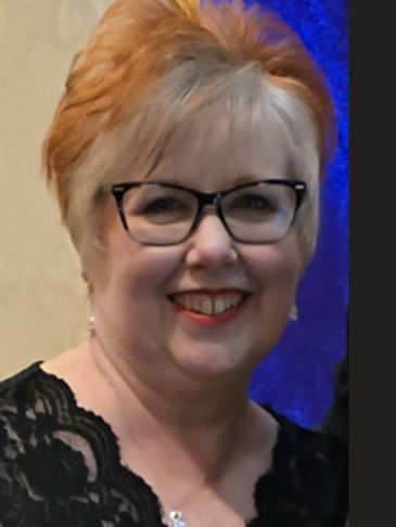 Smiling woman with glasses and reddish hair.