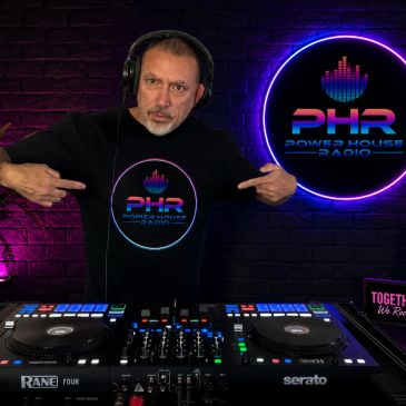 DJ in headphones points to his Power House Radio shirt at a DJ booth.