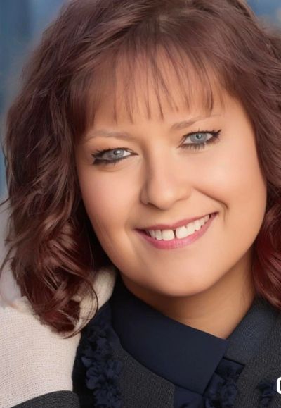 Close-up of a smiling woman with curly hair and light blue eyes.