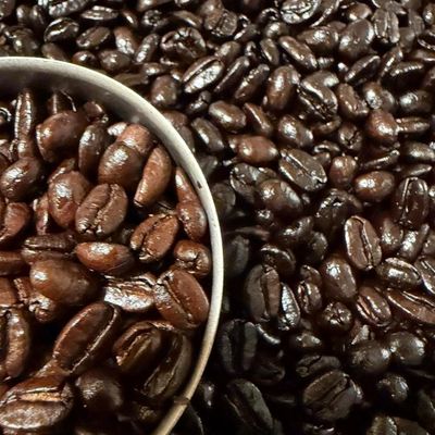 Close-up of shiny roasted coffee beans in a scoop and scattered around.