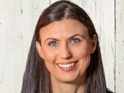 Smiling woman with long dark hair against a rustic wooden background.