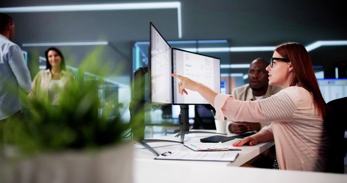 Woman pointing at screen while discussing work with colleague in modern office.