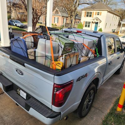 Pickup truck loaded with various household items and secured with netting and straps.